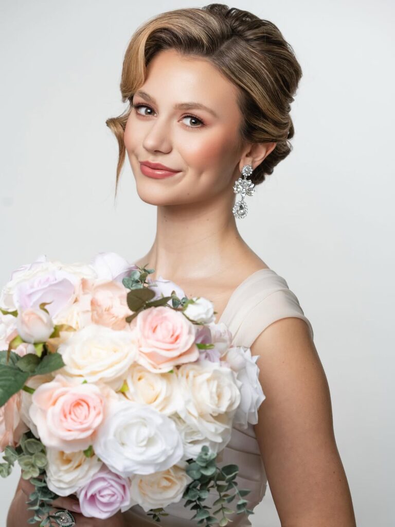 Bridal-style headshot with soft light, floral background, and glamorous earrings